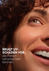 Close-up of a smiling face with warm skin tone, prominent eyelashes, curly brunette hair, and text promoting UV damage prevention.