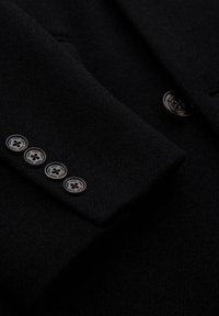 Manga de blazer de lana negra con cuatro botones redondos plateados con un logo, textura suave y diseño ajustado.