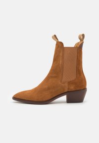 Stivale alla caviglia in suede marrone con punta affilata, pannelli laterali elasticizzati e linguette. Caratterizzato da un tacco impilato e una finitura liscia.