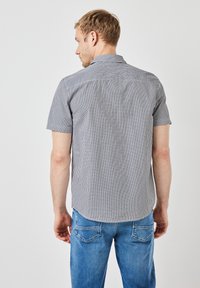 Kortärmad rutiga skjorta i svart och vit, med knäppbar krage och rundad nederkant, kombinerad med blå denimjeans.