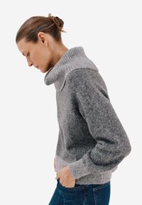 Szary wełniany sweter z szerokim, złożonym kołnierzem i długimi rękawami. Posiada prążkowaną fakturę przy kołnierzu i mankietach, uzupełnioną gładkim korpusem.