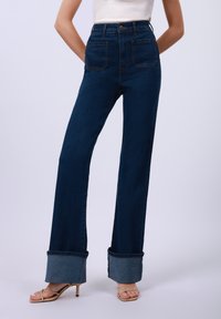 Hoch taillierte dunkelblaue Jeans aus Denim mit weitem Bein und hochgekrempelten Säumen. Der Stoff hat eine glatte Textur, mit Gesäßtaschen und einem Frontknopf.