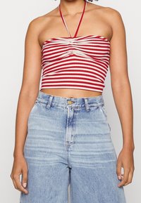 Top corto a righe rosso e crema con davanti arricciato e lacci al collo, abbinato a jeans in denim blu chiaro a gamba larga con chiusura a bottone.