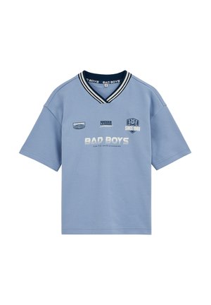 Svetlomodré tričko s krátkym rukávom a výstrihom do V, golier s tmavomodrými pásikmi a bielym textom "BAD BOYS," "Soccer League" a "Since 1988" na prednej strane.