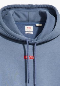 Felpa blu chiaro in cotone con finitura testurizzata, caratterizzata da un logo rosso "LEVI'S" e un cappuccio con cordino. Inclusa etichetta di taglia "M".