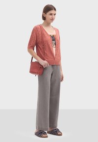 Korallfärgad stickad cardigan med korta ärmar och öppen framsida, ihopparad med en ljusrosa t-shirt med grafik och vida grå byxor. Sandaler med svart och vit rand.