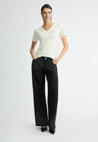 Creme v-udskærmet T-shirt med en lomme, parret med sorte bredbenede jeans med glitrende detaljer på den nederste del. Sorte hæle.