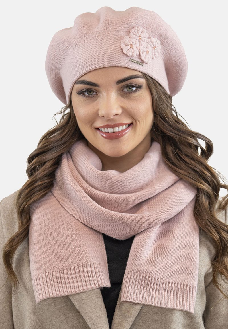 Beret roz tricotat cu accente florale, asortat cu o eșarfă roz similară. Eșarfa are o margine ribb și o textură moale.