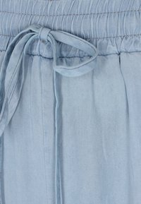 Lichtblauwe denimrokdetail met eenGathered tailleband, verstelbaar strikje en zachte textuur met verticale plooien.