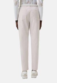 Světle růžové kalhoty z hladké látky s volným střihem, s kapsami vzadu a v kombinaci s bílými teniskami.