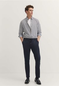 Koszula w paski z podwiniętymi rękawami, zestawiona z ciemnogranatowymi spodniami i czarnymi skórzanymi butami. Gładki materiał o luźnym kroju.