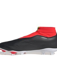 Botas de fútbol negras con un collar de calcetín rojo, parte superior texturizada y suela blanca. Incluye múltiples tacos y detalles en amarillo.