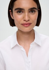 Camicia bianca con colletto in tessuto morbido, caratterizzata da una chiusura con bottoni e un design classico che presenta un aspetto pulito e ordinato.