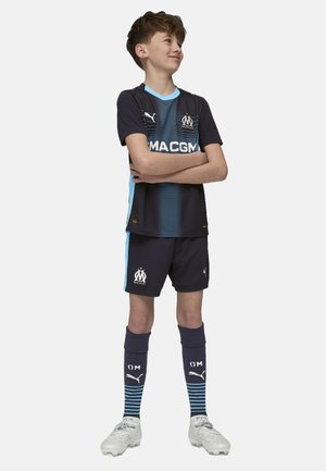 Mörkblå fotbollskit med ljusblå accenter, med logotyp, randiga strumpor och vita fotbollsskor. T-shirt med korta ärmar i ett ventilerande material.