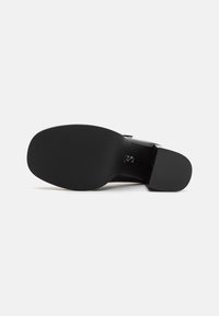 Sola di una scarpa nera con tacchi alti, dal profilo liscia e arrotondata. Gomma testurizzata per la presa, con un discreto emblema del marchio vicino al tallone.