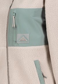 Fleecejacke mit hellbeigem Körper, türkisfarbenem Akzentpanel und Reißverschlusstasche. Verfügt über strukturierten Stoff und ein Markenpatch.