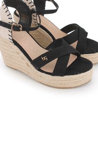 Sandalias de cuña negras con suela de yute, diseño de tiras cruzadas y un acento de logo dorado. Material suave de ante con un detalle de talón trenzado.