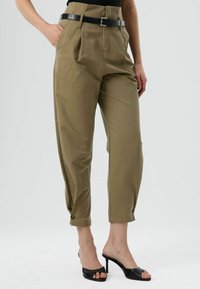 Kaki broek met hoge taille, een losse pasvorm, zijzakken en geruite manchetten met knopen, gecombineerd met zwarte open sandalen met hak.