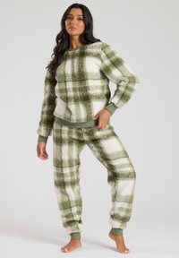 Miękkie zielono-białe loungewear składające się z bluzy z okrągłym dekoltem i spodni z mankietami, wykonane z teksturowanej tkaniny i z prążkowanymi mankietami.