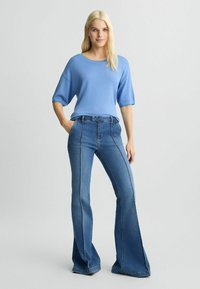 Top scurt albastru cu maneci scurte, cu o croială lejeră, asociat cu blugi din denim albastri cu croi evazat, având cusături vizibile și un design cu talie înaltă.
