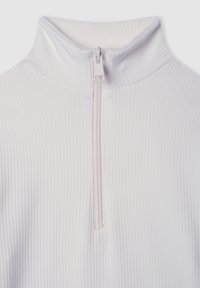 Zbliżenie białej prążkowanej tkaniny z krótkim zamkiem błyskawicznym i wysokim kołnierzem, ukazujące teksturę i detale odzieży.