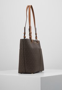 Sac fourre-tout de couleur marron à motif avec une forme structurée, présentant deux poignées en cuir marron, des accents en métal doré et un design à double poche.