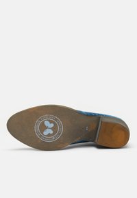 Semelle de chaussure en daim bleu avec un talon en caoutchouc marron, logo circulaire représentant un papillon, taille 37, texture subtile et zones d'usure visibles.