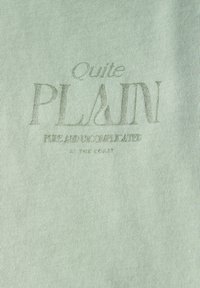 Světle zelená látka s ribrovou strukturou. Uprostřed je text "Docela JEDNODUCHÉ" s dalším malým textem pod ním. Jednoduchý design.