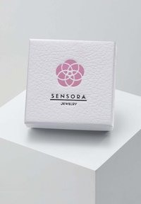 Baltos tekstūros papuošalų dėžutė su rožiniu gėlių logotipu ir juodai atspausdintu "SENSORA JEWELRY". Dėžutė kvadrato formos su lygiu paviršiumi.
