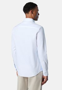 Camicia bianca a maniche lunghe con taglio dritto, chiusura con bottoni e dettagli sui polsini. Tessuto liscio, colletto classico e sottile dettaglio laterale.