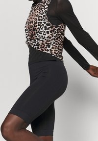 Top bez rukávů s leopardím vzorem a uzlem vpředu, vrstvený přes černou košili s dlouhým rukávem; v kombinaci s černými přiléhavými šortkami.
