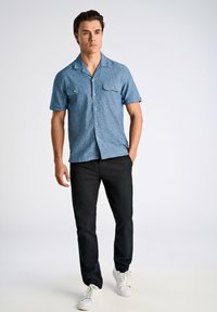Blauw chambray shirt met korte mouwen en twee borstzakken, gecombineerd met zwarte broek en witte sneakers. Glad textuur, casual pasvorm.