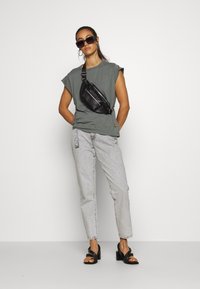Tricou gri cu mânecă scurtă, blugi din denim deschis, rucsac negru, sandale negre cu toc pătrat, ochelari de soare supradimensionați, design minimalist.