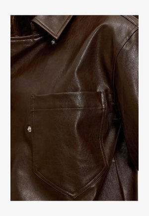 Veste en cuir marron foncé avec une grande poche avant, des coutures visibles, des boutons-pression argentés et un col.