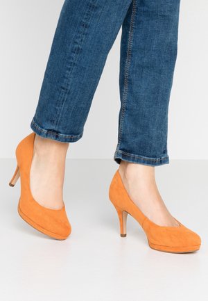 Pomarańczowe zamszowe szpilki z zaokrąglonym noskiem, z zamkniętym tyłem i średniej wysokości obcasem. W zestawie z dżinsami.