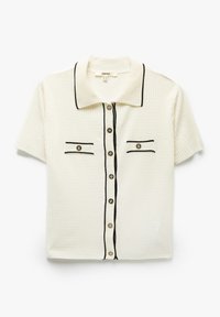 Polo a maniche corte in tessuto crema texturizzato, con finiture nere, due tasche frontali e cinque bottoni al centro.