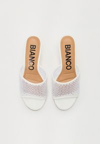 Sandalias de slide abiertas en la parte delantera, de color blanco, con una tira de malla blanca, plantilla color beige y la marca "BIANCO" en negro. Suela plana y textura suave.