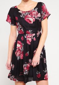 Robe fleurie à manches courtes en tissu noir, ornée de grandes roses roses et rouges, avec un col rond et une taille cintrée.
