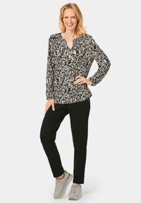Zwarte en crèmekleurige blouse met een patroon, lange mouwen, een V-halslijn, gecombineerd met zwarte broek en beige sneakers. Soepele stof.