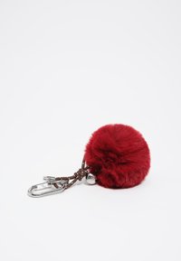Czerwony pompon z futra na breloczku z brązowym sznurkiem, srebrnymi akcesoriami i dekoracyjnym metalowym dzwonkiem. Miękka struktura i okrągły kształt.