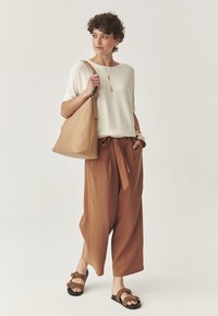 Creme strikket top, brune linned højtaljede bukser med bånd, tan læder skuldertaske, brune sandaler med guldspænder, struktureret stof.