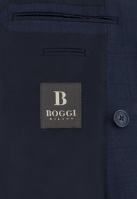 Innenfutter eines marineblauen Blazers mit eingenähtem Etikett mit der Aufschrift "B Boggi Milano" und einem passenden Knopf mit demselben Text.