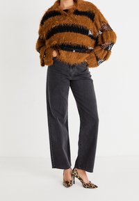 Fuzzy brun och svart randig tröja, högmidjade svarta jeans och leopardmönstrade klackar, vilket skapar en texturerad och lager-på-lager outfit.