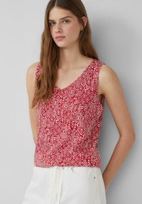 Top rosso senza maniche con un motivo geometrico bianco, scollatura a V e vita arricciata. Realizzato in tessuto leggero.