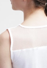 Top bianco senza maniche caratterizzato da un pannello in rete sul retro, che combina un tessuto liscio con un design testurizzato a maglia aperta.