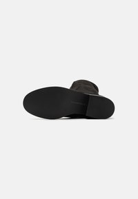 Black suede ankle boot with a smooth texture, round toe, and flat rubber sole. Subtle branding embossed on the sole.