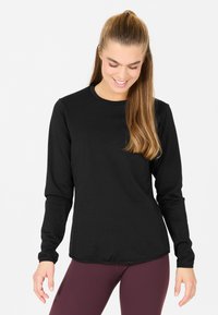 Langärmliges schwarzes Shirt aus strukturiertem Stoff mit rundem Ausschnitt und taillierter Passform, kombiniert mit dunkelmaronen Leggings.