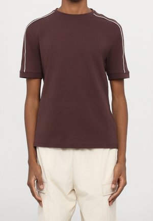 Brun bomuld t-shirt med korte ærmer og opsmøgede manchetter. Har hvide kontrastsømme langs skuldersømmene. Minimalistisk design.