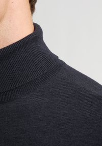 Granatowy sweter z golfem z dzianiny, z prążkowanym dekoltem i gładką teksturą. Zbliżenie ukazuje detale szycia i dekoltu.