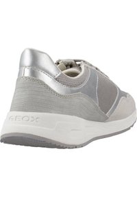 Zapatilla gris con parte superior de malla texturizada y acentos plateados brillantes. Presenta un diseño curvado, cuello acolchado y suela blanca con un patrón antideslizante.